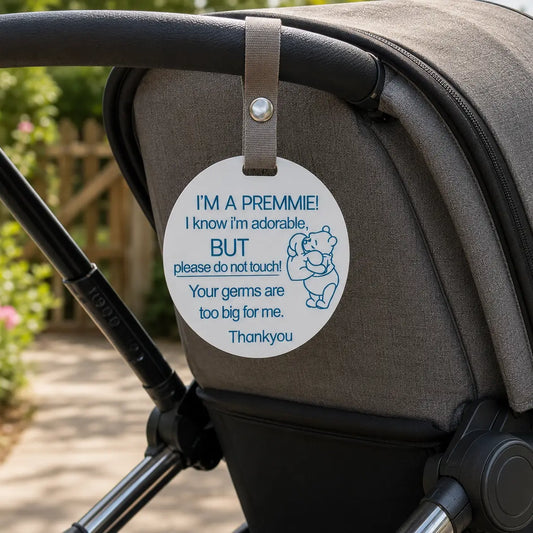 Baby stroller with a tag reading 'I'm a preemie! Please do not touch' on a blurred outdoor background.