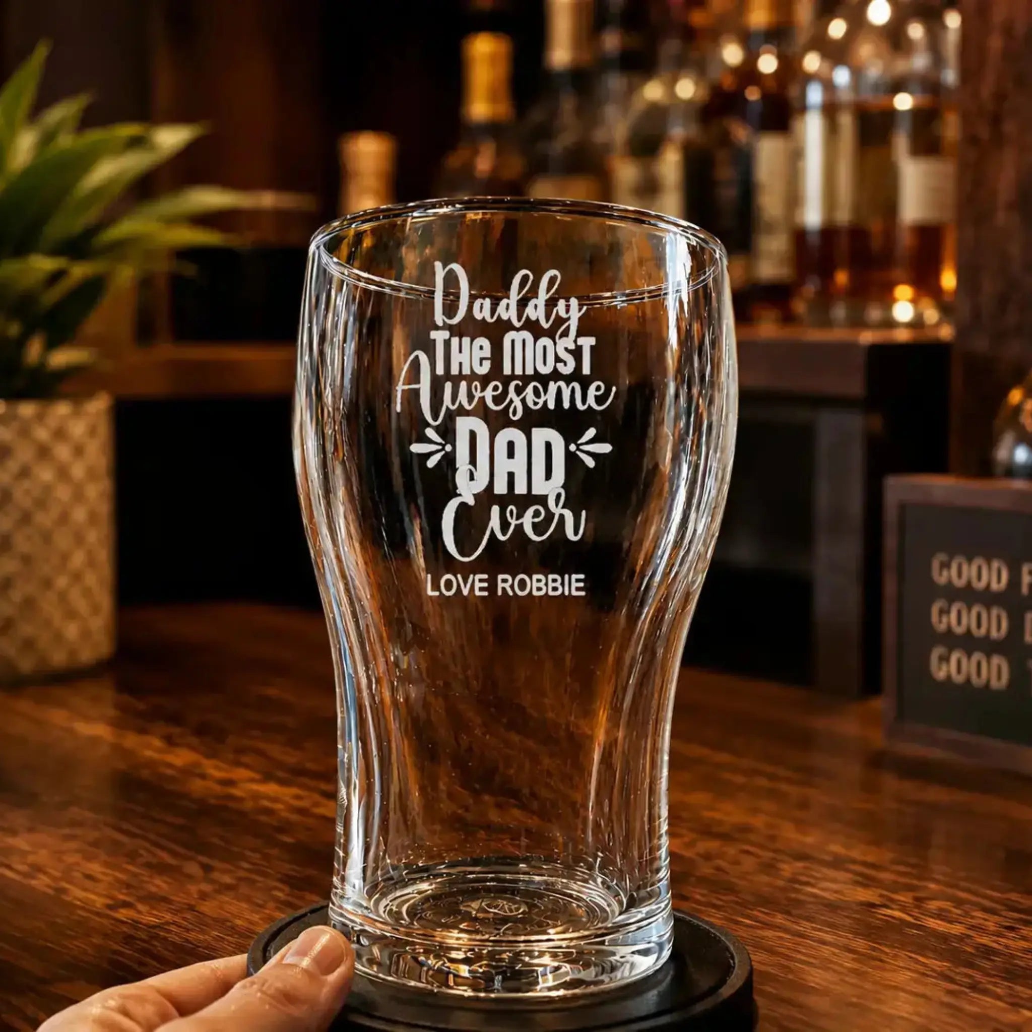 Personalised engraved beer glass for Dad displayed in a stylish home bar setting, featuring the quote “Daddy The Most Awesome Dad Ever” with custom name engraving on a clear pint glass.